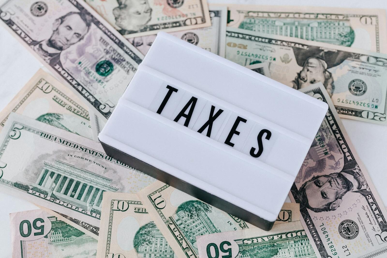From above of white retro lightbox with TAXES inscription placed on pile of USA dollar bills on white surface