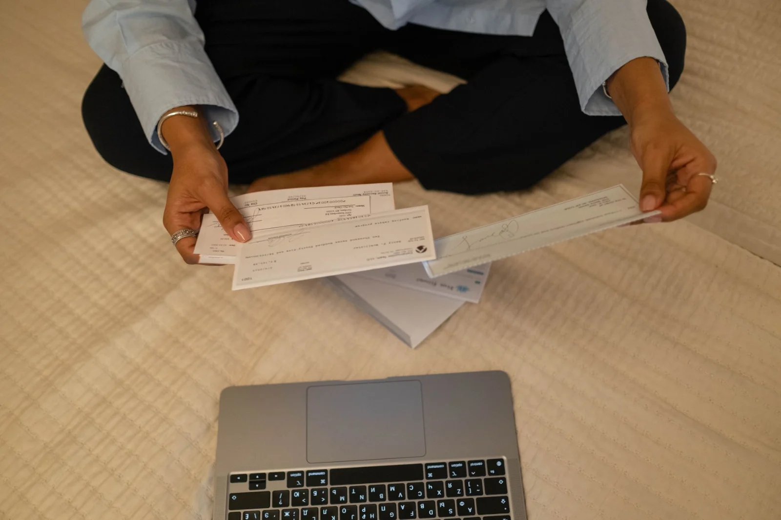 Compounding of Cheque Dishonour Cases Under - Close-up of hands holding cheques beside a laptop indoors for financial tasks.