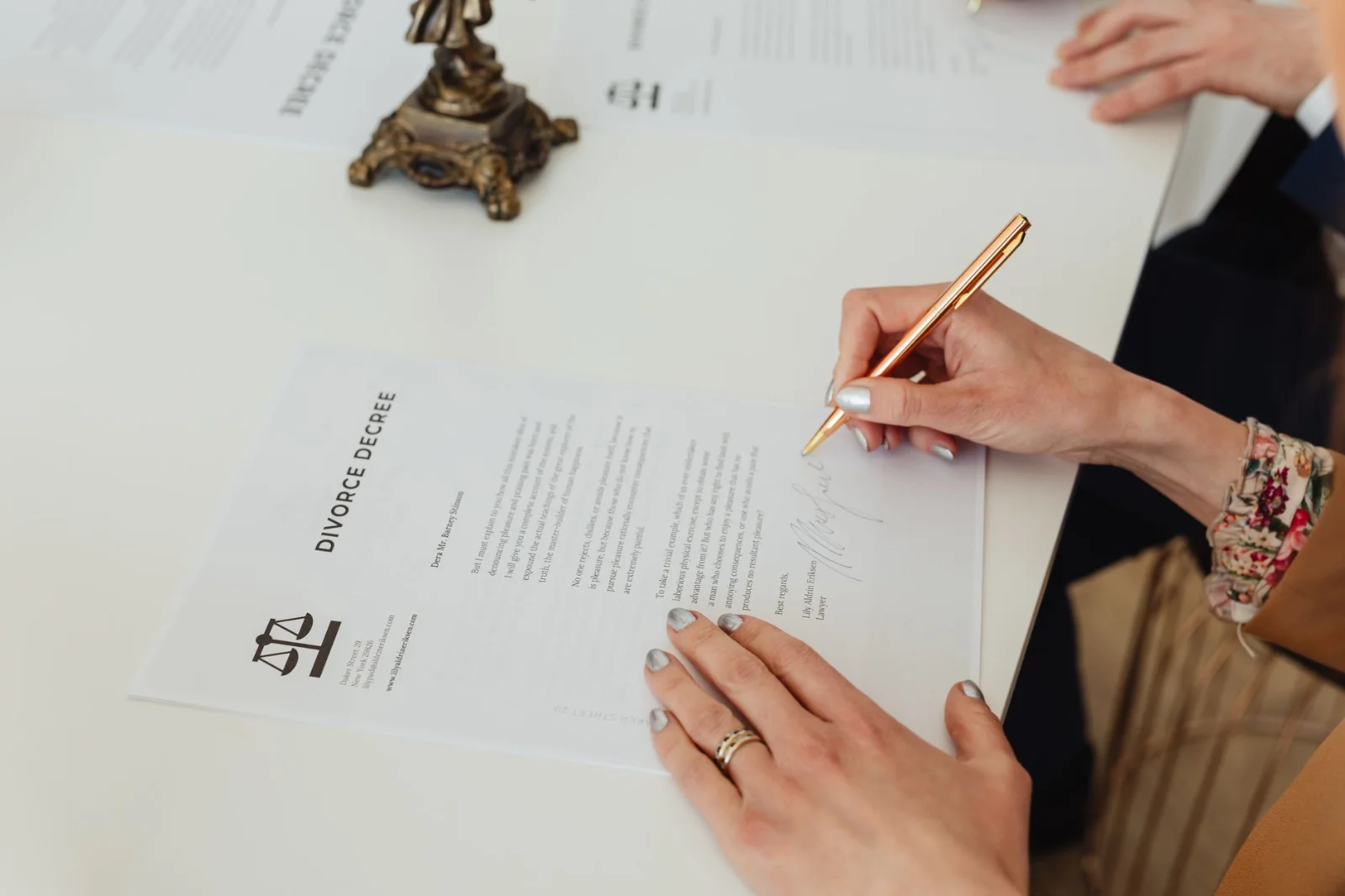 Consent As The Cornerstone Of Arbitration: - Close-up of hands signing a divorce decree document on a desk, showcasing legal