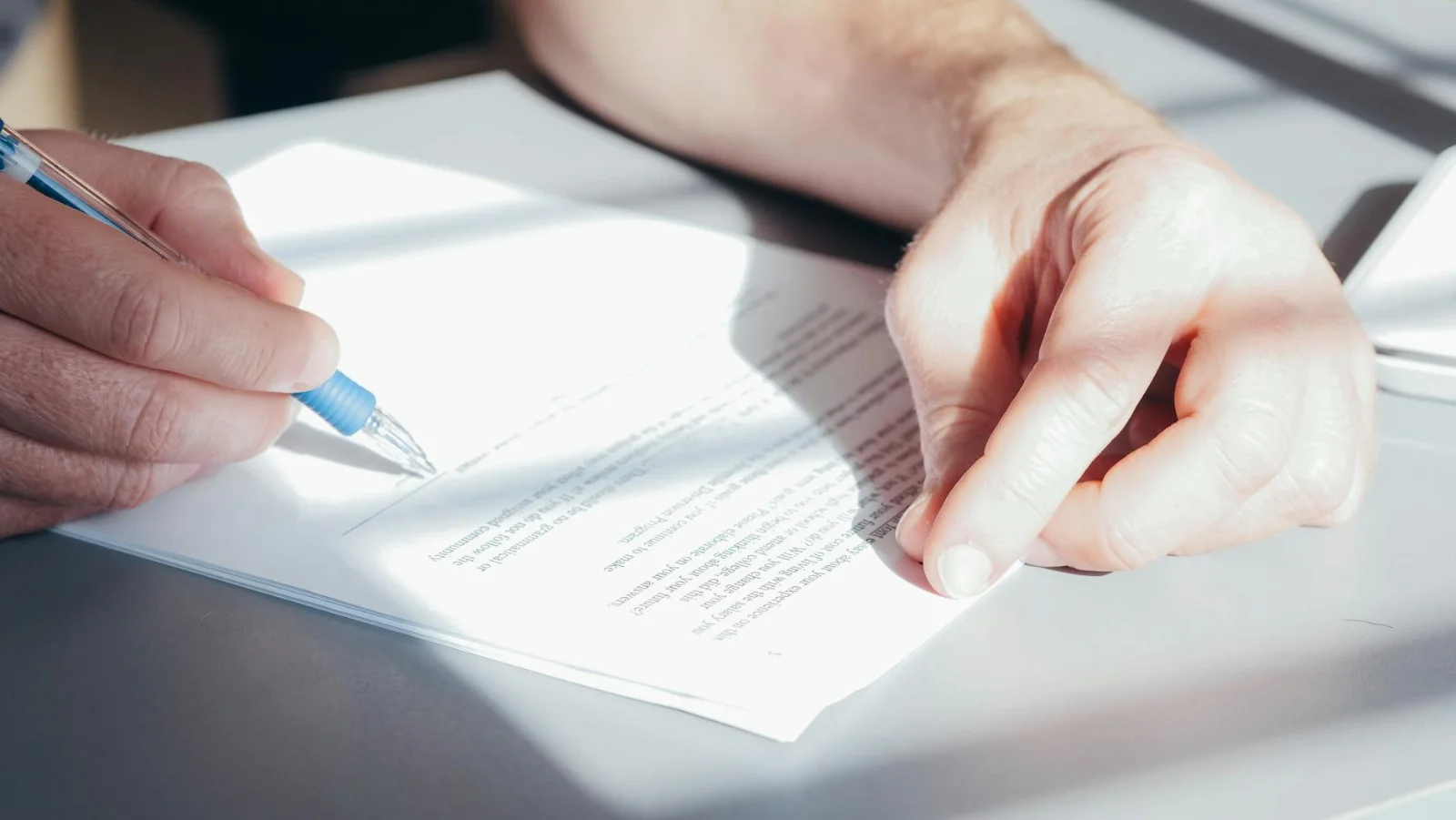 Defamation under the IPC and Bharatiya - Hands signing a contract with a blue pen, close-up view.