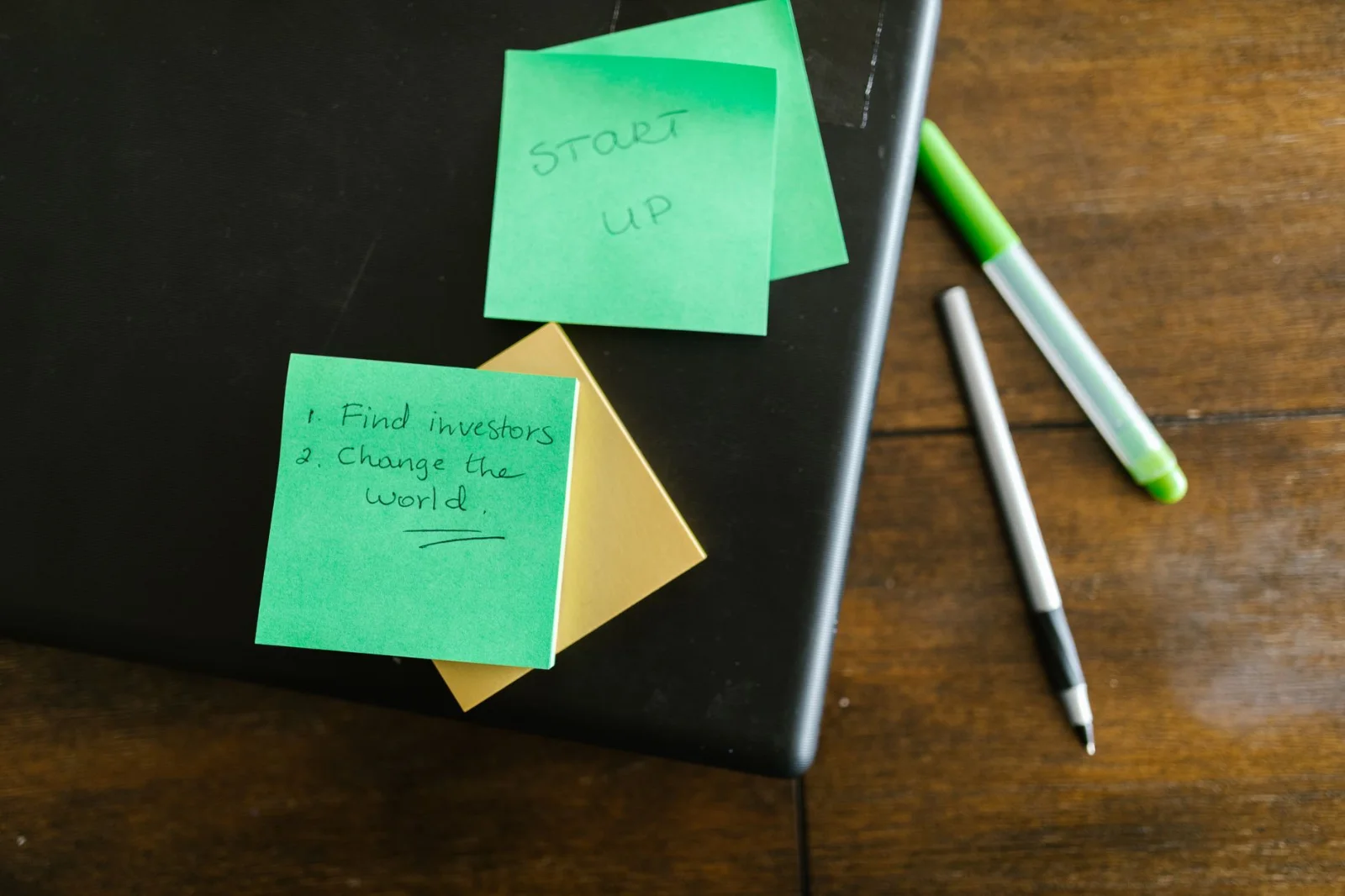 ESOP Pool Before Funding: ESOP Trust - Green sticky notes with startup goals on a wooden desk with pens.