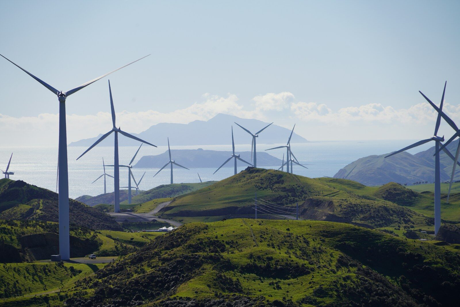 Wind turbines on a green grassy hill overlooking the ocean