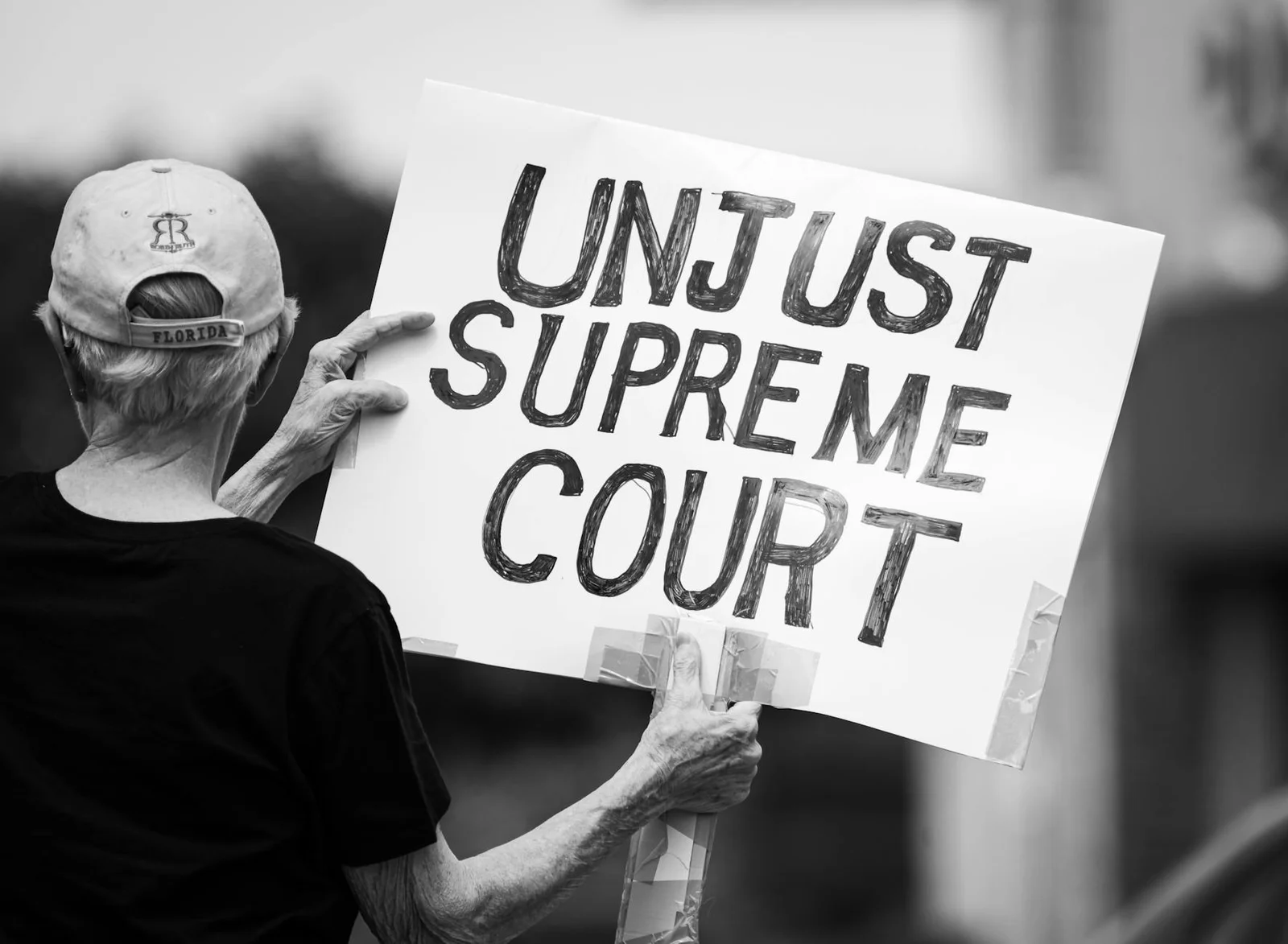 Black and white photo of a protester holding a sign saying 'Unjust Supreme Court' during a demonstration.