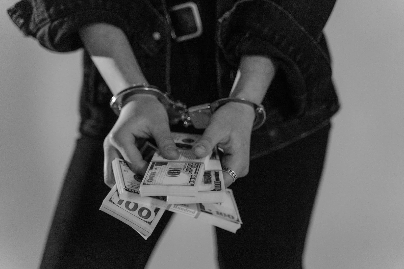 pmla bail jurisprudence prolonged incarceration article - Black and white image of a handcuffed person holding bundles of US