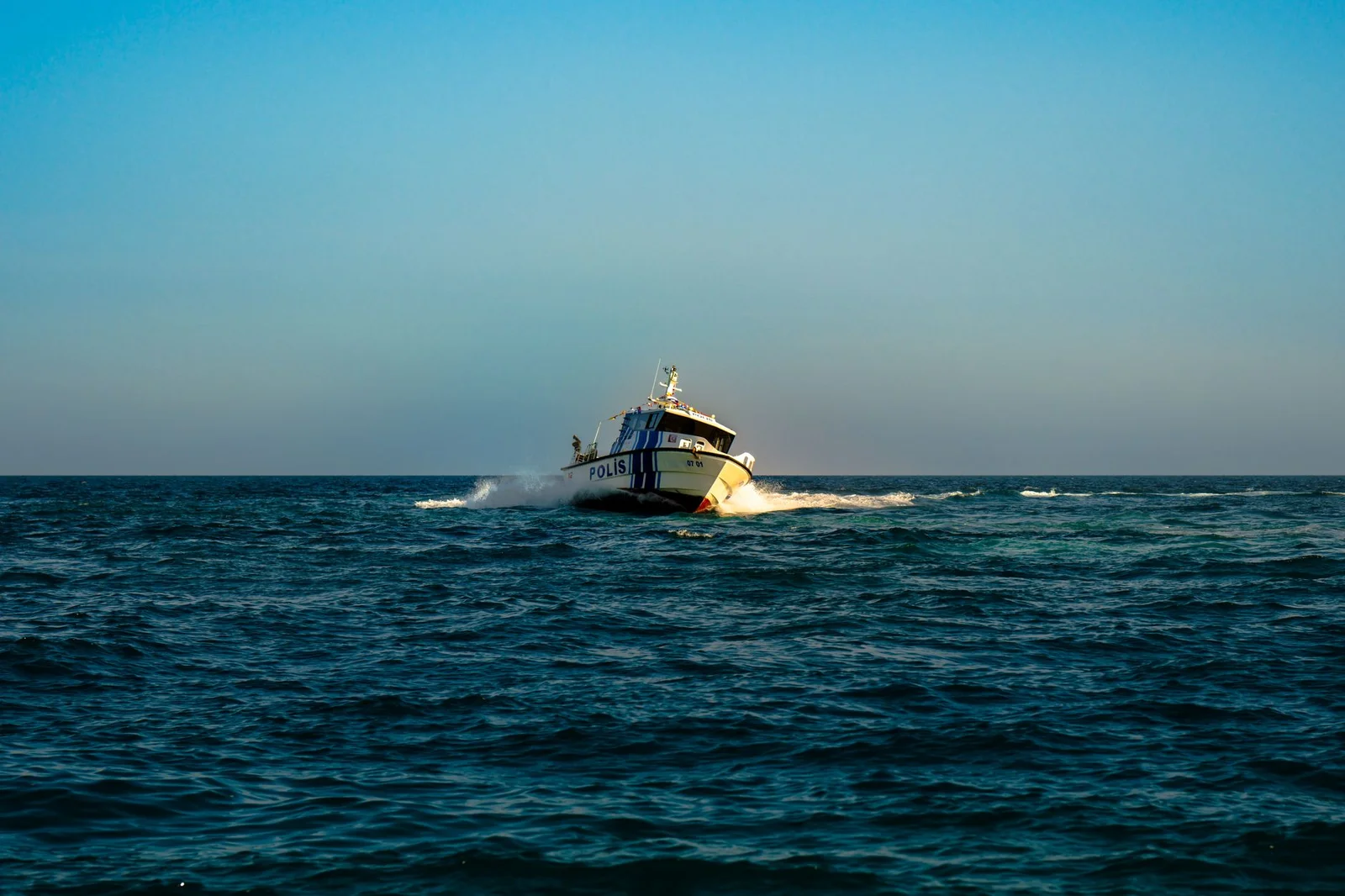 maritime claim enforcement india - Arbitration - A police boat speeds across the open sea under a clear blue sky.